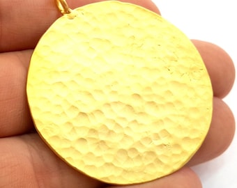 Può includere: Un ciondolo rotondo dorato con una texture martellata. Il ciondolo ha un anello nella parte superiore per attaccarlo a una catena.