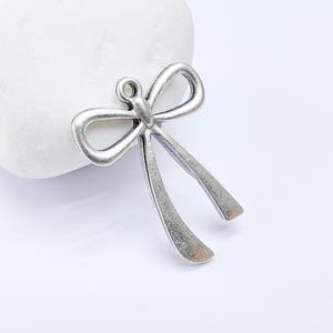 Könnte beinhalten: Silberfarbener Metall-Schleifenanhänger mit einer Öse zum Anbringen an Schmuck oder Bastelarbeiten.