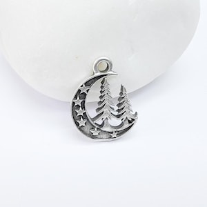 May include: A silver charm featuring a crescent moon with stars and two stylized pine trees inside the moon.