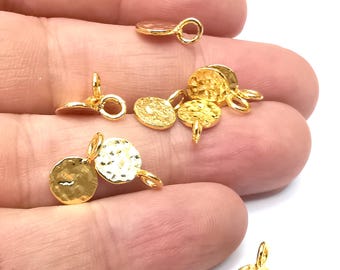 May include: Several small, gold-colored metal charms with a hammered texture and a loop for attaching to jewelry. The charms are round and have a small post on the bottom. The charms are scattered on a white background.