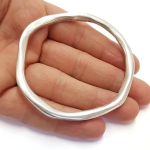 May include: A silver bangle bracelet with a smooth, rounded surface. The bracelet is open and has a simple, minimalist design.