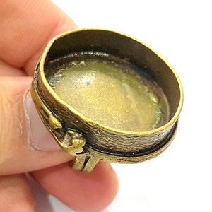 Puede incluir: Un anillo de tono dorado con un engaste redondo abierto. El anillo está diseñado para sujetar una piedra cabujón u otro elemento decorativo.