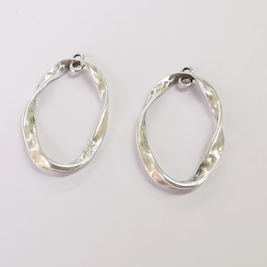May include: Two silver twisted oval shaped hoops with a small loop at the top for hanging.