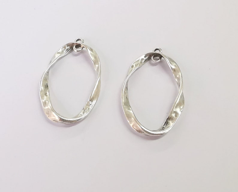 May include: Two silver twisted oval shaped hoops with a small loop at the top for hanging.