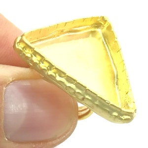 May include: Gold-toned triangular ring setting with a textured edge and a clear glass insert.