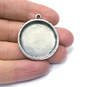 Könnte beinhalten: Silberner Anhänger mit einer runden, glatten, leeren Oberfläche. Der Anhänger hat einen strukturierten Rand.