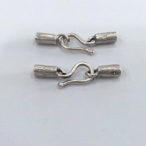 May include: Two silver-toned metal clasps with a hook and loop design. Each clasp has a cylindrical barrel with a textured surface.
