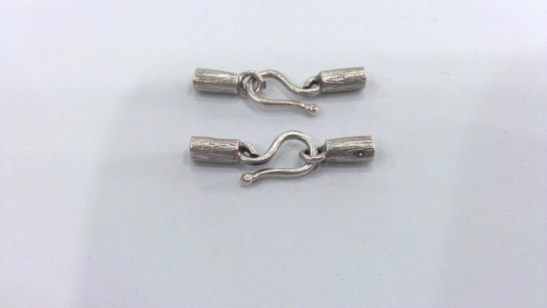 May include: Two silver-toned metal clasps with a hook and loop design. Each clasp has a cylindrical barrel with a textured surface.