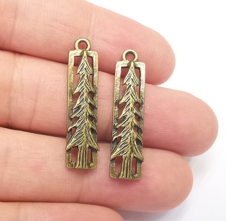 K&ouml;nnte beinhalten: Zwei antike goldfarbene Metall-Anh&auml;nger in Form von Tannenb&auml;umen. Jeder Anh&auml;nger hat oben eine &Ouml;se zum Anbringen an einer Halskette, einem Armband oder anderem Schmuck.
