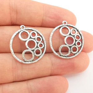 May include: Two silver-toned metal circle pendant charms with a cutout design of overlapping circles. The charms have a textured surface and a loop at the top for attaching to jewelry.