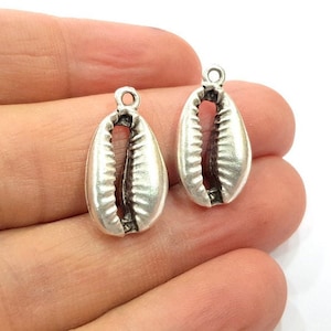 May include: Two silver-toned cowrie shell charms with a loop at the top for attaching to jewelry or crafts.