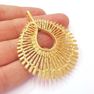 May include: A gold-toned pendant with a sunburst design. The pendant features a large, open circle in the center with radiating lines extending outward.