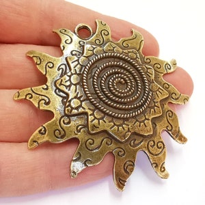 K&ouml;nnte beinhalten: Ein goldfarbener Metall-Sonnenanh&auml;nger mit einem Spiraldesign in der Mitte und filigranen Details an den R&auml;ndern.