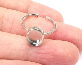 Könnte beinhalten: Ein verstellbarer Silberring mit einer runden, flachen Zargenfassung für einen Cabochon.