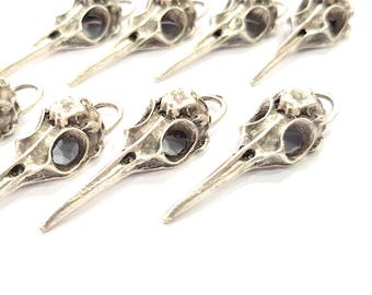 May include: A set of ten silver bird skull charms with a detailed design. Each charm has a small loop at the top for attaching to jewelry or other crafts.