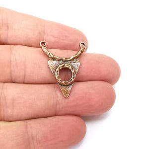 May include: A copper triangle pendant with a textured surface and a circular opening in the center. The pendant has two loops at the top for attaching a chain.
