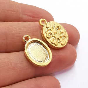 May include: Two gold-toned metal oval charms. One charm has a raised, ornate design. The other charm is plain and has a smooth surface.