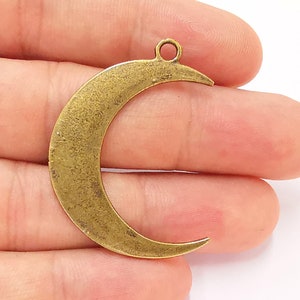 Op de afbeelding: Een gouden metalen halve maan bedel met een lus aan de bovenkant om te bevestigen aan sieraden of andere knutselwerkjes.