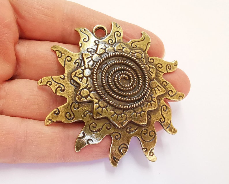 K&ouml;nnte beinhalten: Goldfarbener Metall-Sonnenanh&auml;nger mit einem Spiraldesign in der Mitte und filigranen Details an den R&auml;ndern.