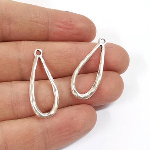 May include: Two silver teardrop-shaped earring blanks with a hammered texture. The blanks have a small loop at the top for attaching earring wires.