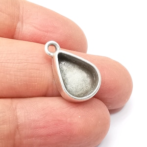 May include: Silver teardrop pendant with a round opening for resin or other materials. The pendant has a loop at the top for attaching to a chain or cord.