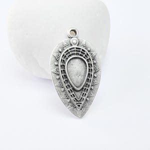 Puede incluir: Pendiente de plata con forma de lágrima y un intrincado diseño geométrico. El pendiente tiene un acabado liso y pulido y un delicado patrón calado.