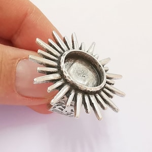 May include: Silver ring with a sunburst design and a round, open bezel for a cabochon stone.