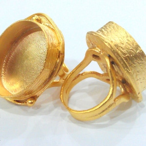 May include: Two gold-tone rings with a round, open setting. The rings are made of a textured metal and have a vintage style.