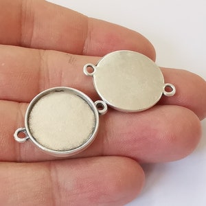 May include: Two silver-toned metal round pendant trays with a smooth, slightly textured surface. Each tray has a loop on the side for attaching a chain or cord.