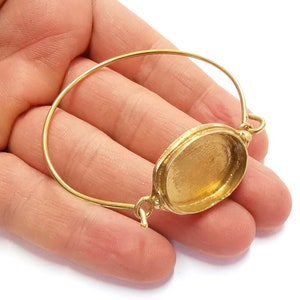 Peut inclure: Un bracelet jonc doré avec un bézel rond à face ouverte. Le bézel est fixé au jonc par une petite boucle décorative.