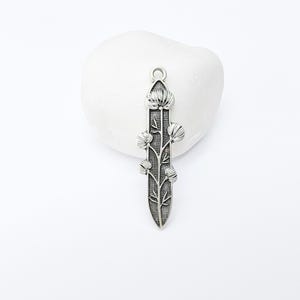 Op de afbeelding: Zilverkleurige hanger met een bloemmotief. De hanger heeft een centrale stengel met gestileerde bloemen en bladeren. De hanger staat tegen een witte achtergrond.
