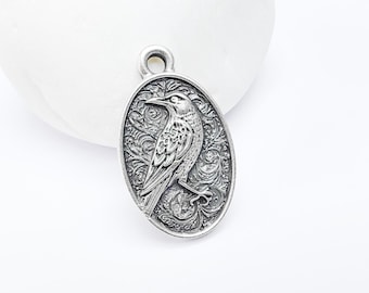 May include: Silver oval charm with an intricate design featuring a bird with detailed feathers and a floral background.