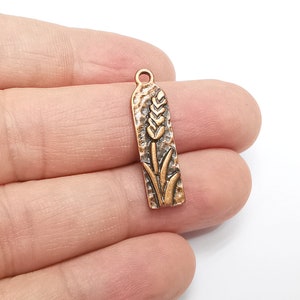 May include: A copper-toned metal charm with a wheat stalk design. The charm has a textured surface and a loop at the top for attaching to a necklace or bracelet.