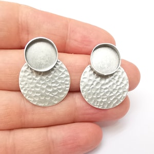 May include: A pair of silver earrings featuring a hammered round disc with a round bezel setting on top.