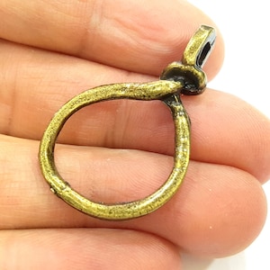 May include: A gold-toned metal loop with a knotted design. The loop is open and has a small metal loop at the top.