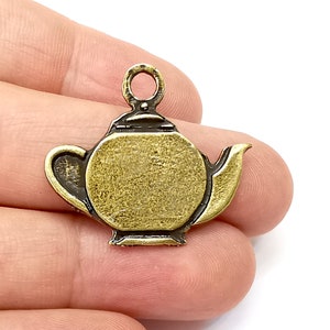 Può includere: Un ciondolo a forma di teiera in metallo dorato con un anello in cima per attaccarlo a una collana o un braccialetto. Il ciondolo è dettagliato con un beccuccio e un manico.