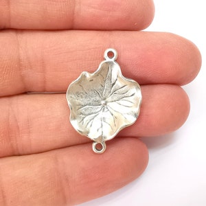 Könnte beinhalten: Silberfarbener Metall-Anhänger in Form eines Blattes mit detailliertem Design. Der Anhänger hat zwei Sprungringe zum Anbringen an Schmuck oder anderen Bastelarbeiten.