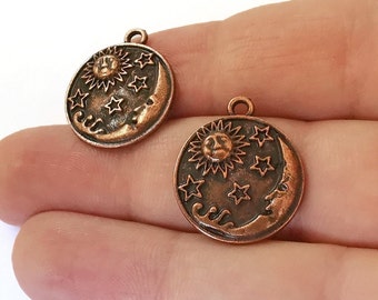 May include: Two copper-colored charms featuring a sun and moon design with stars. The charms are round and have a detailed design.
