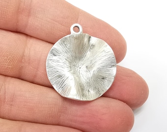 May include: Silver pendant with a round, textured, and slightly concave design. The pendant has a small loop at the top for attaching a chain.
