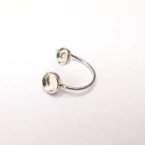 Puede incluir: Anillo de plata con dos engastes redondos. Los engastes están vacíos y listos para ser rellenados con piedras u otros adornos.