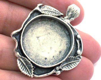 May include: Silver-toned pendant setting with a round, open bezel and a leafy design. The setting is designed to hold a round cabochon.