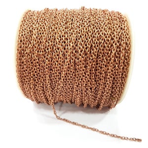 Könnte beinhalten: Eine Spule mit kupferfarbener Kette. Die Kette besteht aus kleinen, ovalen Gliedern und ist eng um eine weiße Spule gewickelt. Die Kette hat eine warme, metallische Farbe und scheint neu zu sein.