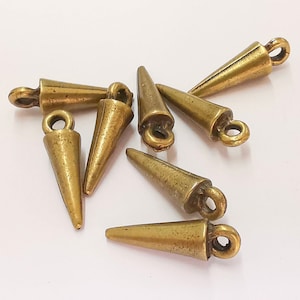 May include: A group of six gold-toned metal cone-shaped charms with a loop at the top. The charms are arranged in a cluster on a white surface.
