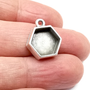 May include: Silver hexagon pendant with a clear, round, open space in the center. The pendant has a loop at the top for attaching to a chain or cord.