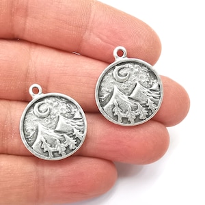 May include: Two silver-toned metal charms featuring a mountain scene with a crescent moon. Each charm is round and has a loop for attaching to a necklace or bracelet.