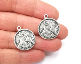 May include: Two silver-toned metal charms featuring a mountain scene with a crescent moon. Each charm is round and has a loop for attaching to a necklace or bracelet.