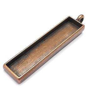 May include: A rectangular copper-colored metal pendant with a loop at the top for hanging. The pendant has a rectangular opening in the center, suitable for adding resin or other materials.