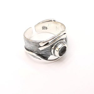 Könnte beinhalten: Ein verstellbarer Silberring mit einer strukturierten Band und einem runden Design in der Mitte. Der Ring hat einen 925 Stempel auf der Innenseite.