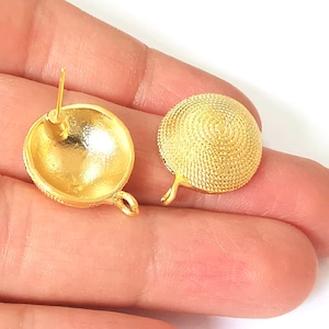 May include: A pair of gold-tone metal earring posts with a round, textured design. The earrings have a post and a small loop on the back.