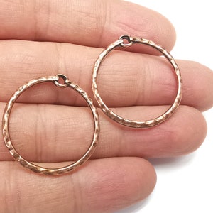 May include: Two hammered copper hoop earrings. The hoops are round and have a textured surface.